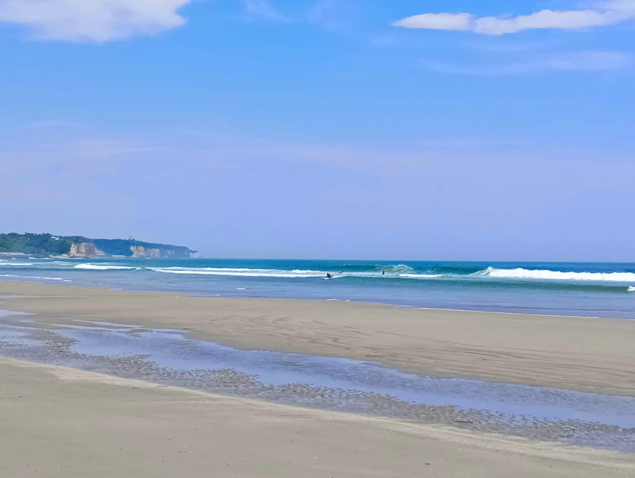 岩沢海水浴場の砂浜と海。火力発電所を背景にサーファーが集まる海水浴場
